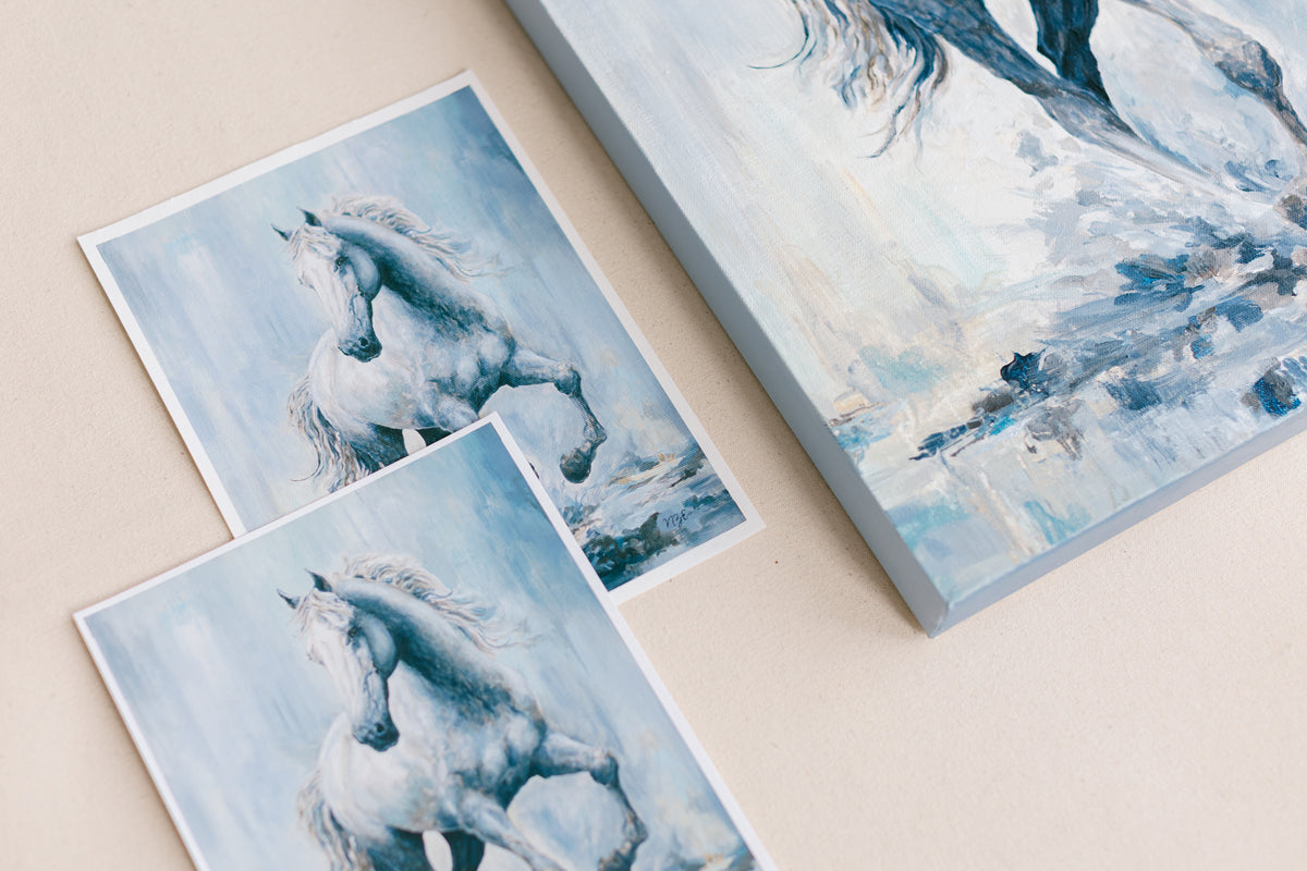 Three art prints, two fine art paper giclée prints and one stretched giclée art print painting featuring a white horse displayed on a light beige surface. The featured art is titled, Chasing Light, a print from mixed-media artist Nicole Z Edwards.